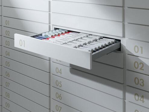 Detailaufnahme von schmalen weißen Medikamentenschubläden mit dezenter Nummerierung und sichtbarer Medikamentenaufteilungen.