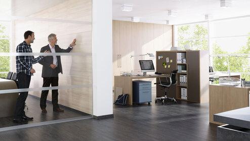 Impression eines Büros mit abgeschlossenem Raum mit Glaswand und offener Bürogestaltung.