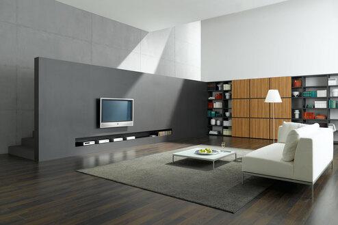 Offene Wohnraumimpression mit grauer TV-Trennwand zur Treppe und Einbauregal aus Holz und weißem Sofa